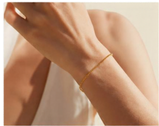 Steala permanent jewelry postcard 1 - Steala LLC Fine Art Accessories Close-up of a forearm with a thin gold bracelet on the wrist, wearing a light sleeveless top in the background.